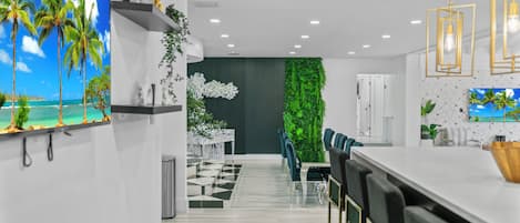 A modern kitchen with a white countertop, bar stools, and a green vertical garden wall.