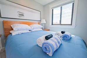 Ett hotellrum med en säng, kuddar, ett nattduksbord, en lampa, ett fönster med utsikt och handdukar på sängen.