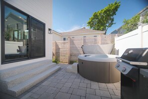 A patio with a hot tub, grill, and steps leading to a glass door. - Sandscape Retreat | New Build | Spa + Beach Walk (Old Orchard Beach)