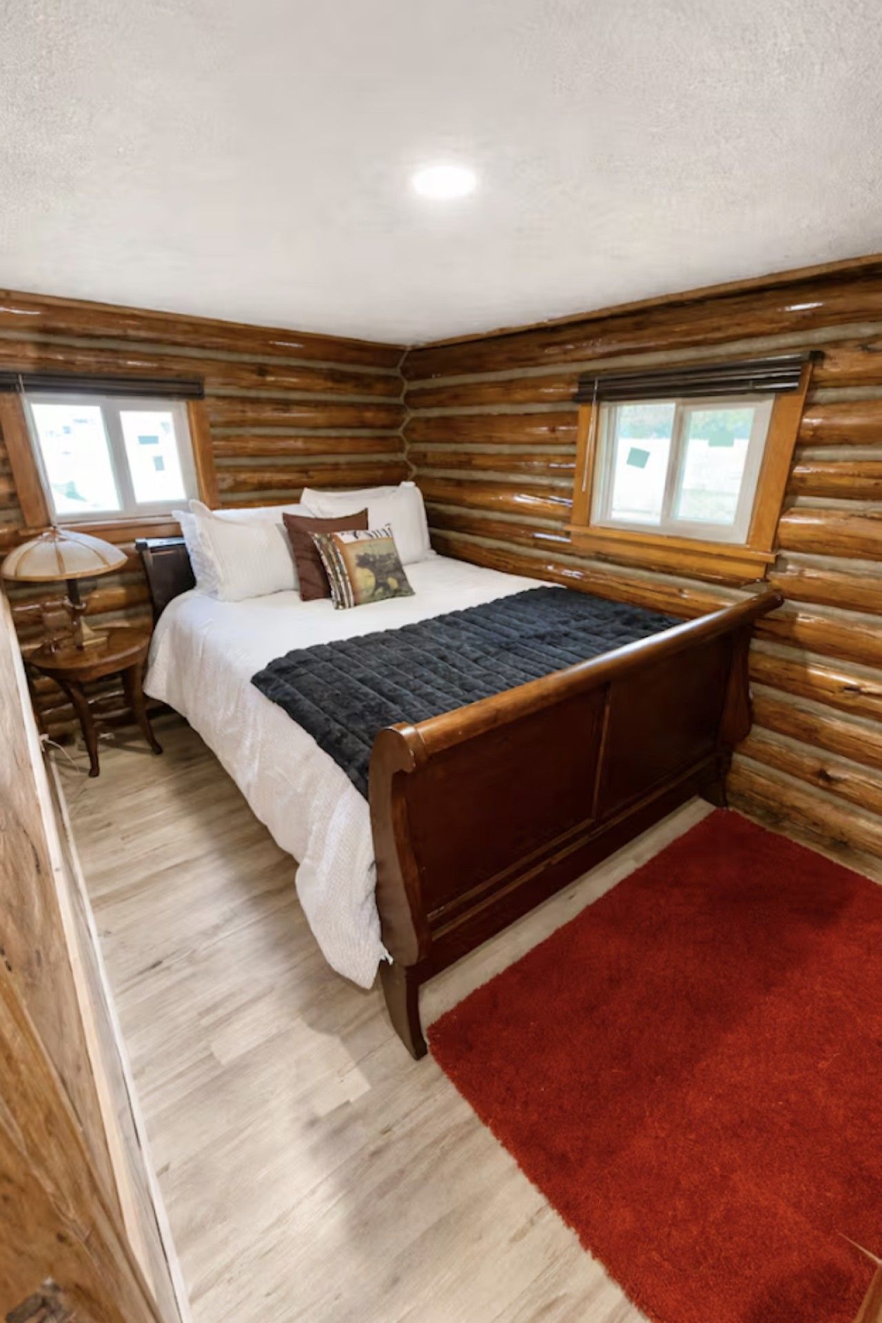 A log cabin-style bedroom with a wooden bed, a nightstand, and a red rug.
