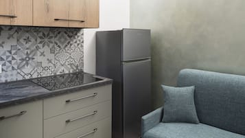 Eine kompakte Küche mit Kühlschrank, Backofen und einem grauen Sofa.