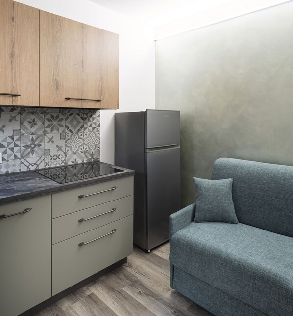Eine kompakte Küche mit Kühlschrank, Backofen und einem grauen Sofa.