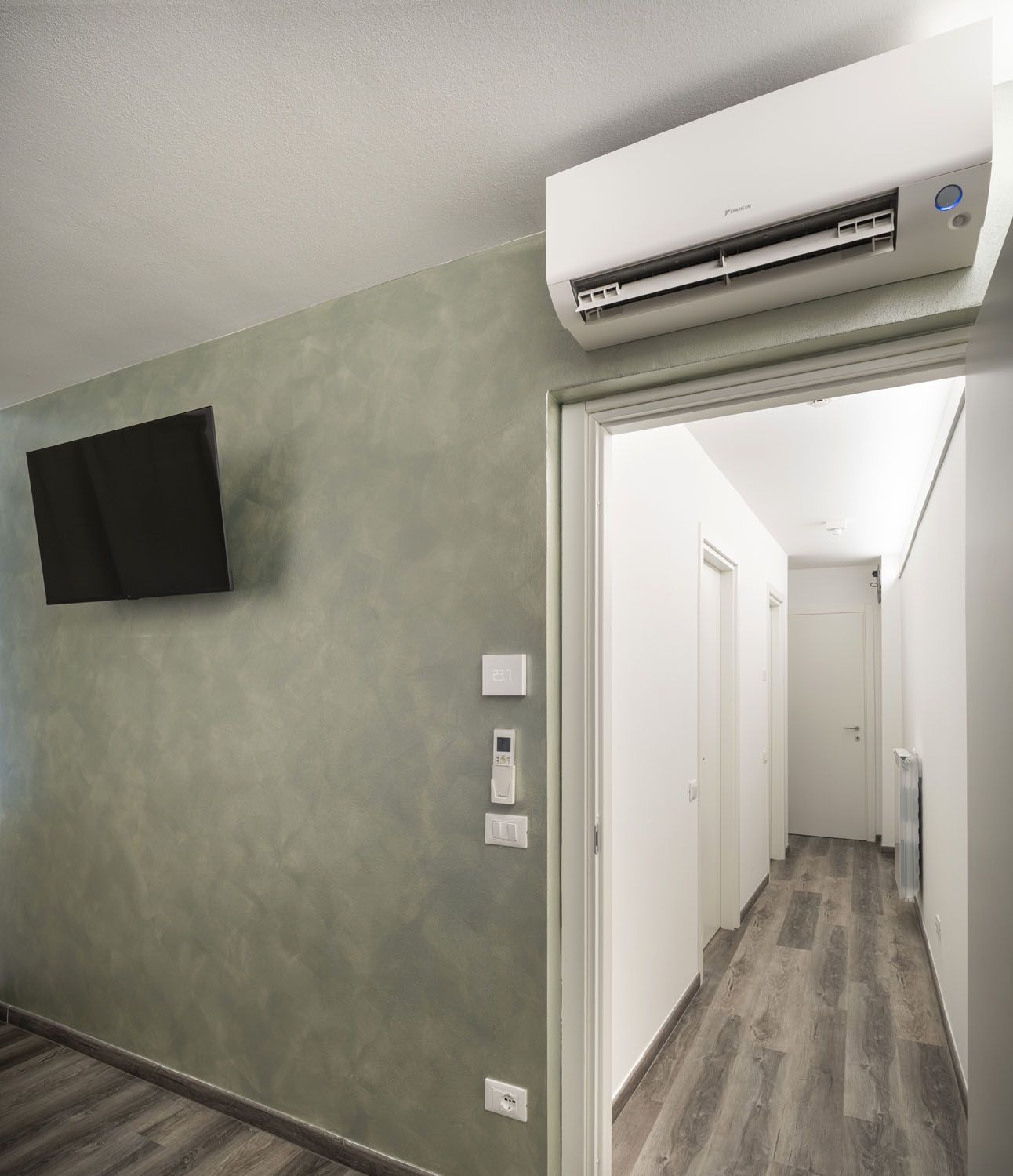 Ein Flur mit einer Wandklimatechnik, einem Flachbildfernseher an der Wand und einer Tür zu einem weiteren Zimmer.