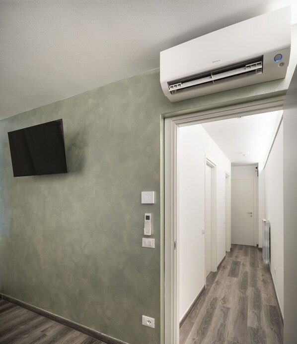 A hallway with a mounted air conditioner, a flat-screen TV on the wall, and a door leading to another room.