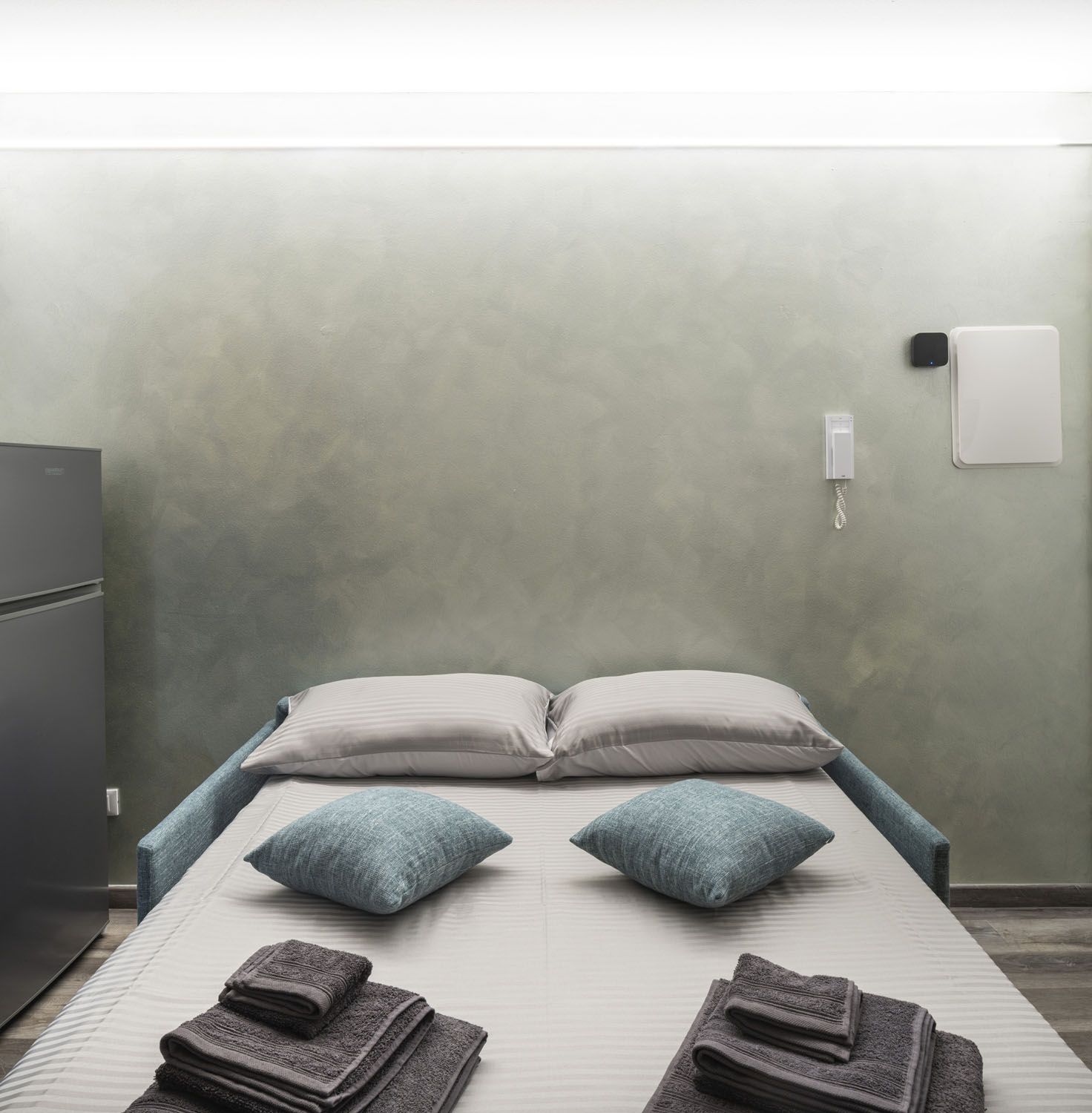 Ein Einzelbett mit zwei Kissen, ein Nachttisch mit Lampe und ein an der Wand befestigtes Telefon.