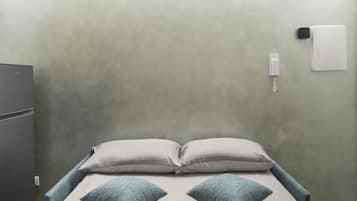 Ein Einzelbett mit zwei Kissen, ein Nachttisch mit Lampe und ein an der Wand befestigtes Telefon.