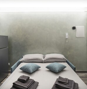 A single bed with two pillows, a bedside table with a lamp, and a wall-mounted phone.