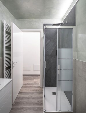 Ein modernes Badezimmer mit bodengleicher Dusche, einem weißen Waschtisch und einer Tür zu einem anderen Raum.