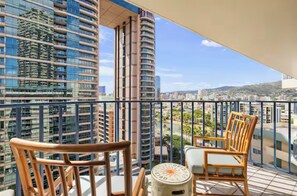A balcony with two wooden chairs and a small round table, overlooking a cityscape with high-rise buildings. - Peaceful Waikiki Apartment - 2B1B with Free Parking (Honolulu)