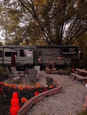 Una vehículo recreativo (RV) estacionado en un jardín con un sendero de grava, rodeado de sillas y una pequeña mesa.