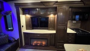 Interior de una caravana compacta con centro de entretenimiento integrado, chimenea y pequeña cocina.