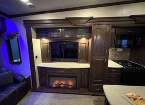 Interior de una caravana compacta con centro de entretenimiento integrado, chimenea y pequeña cocina.