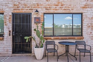 Een bakstenen gebouw met een metalen poort, een cactus in een pot en twee metalen stoelen met een tafel.