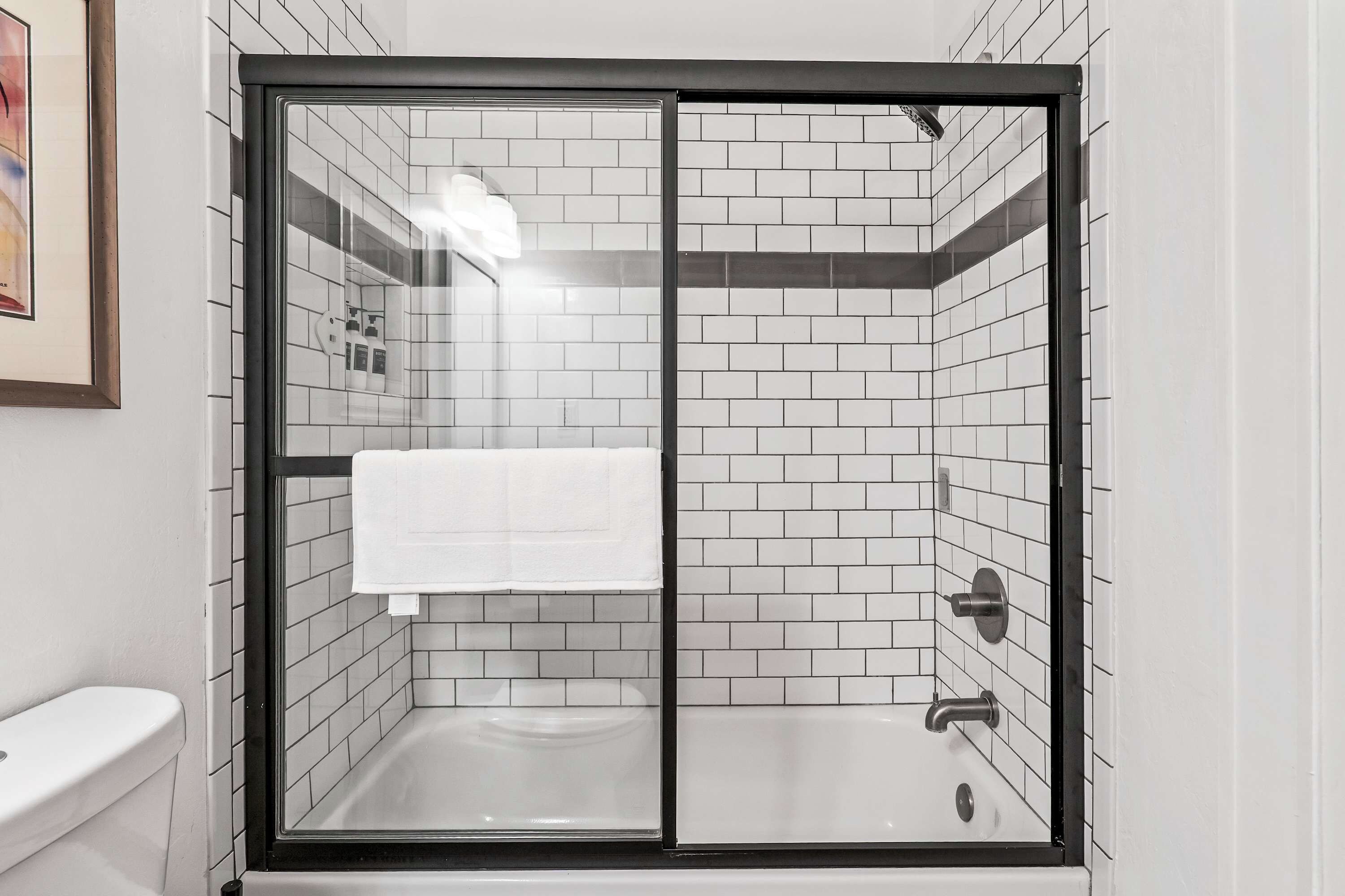 A bathroom with a glass-enclosed shower, white tiled walls, and a white toilet.
