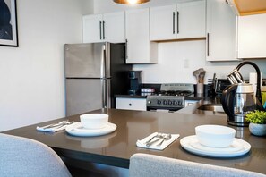 Een moderne keuken met roestvrijstalen apparatuur, witte kastjes en een eethoek met een tafel gedekt voor twee personen.