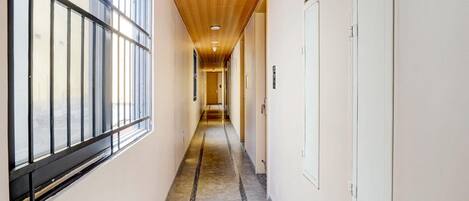 A hallway with a wooden ceiling, large windows on one side, and a concrete floor.