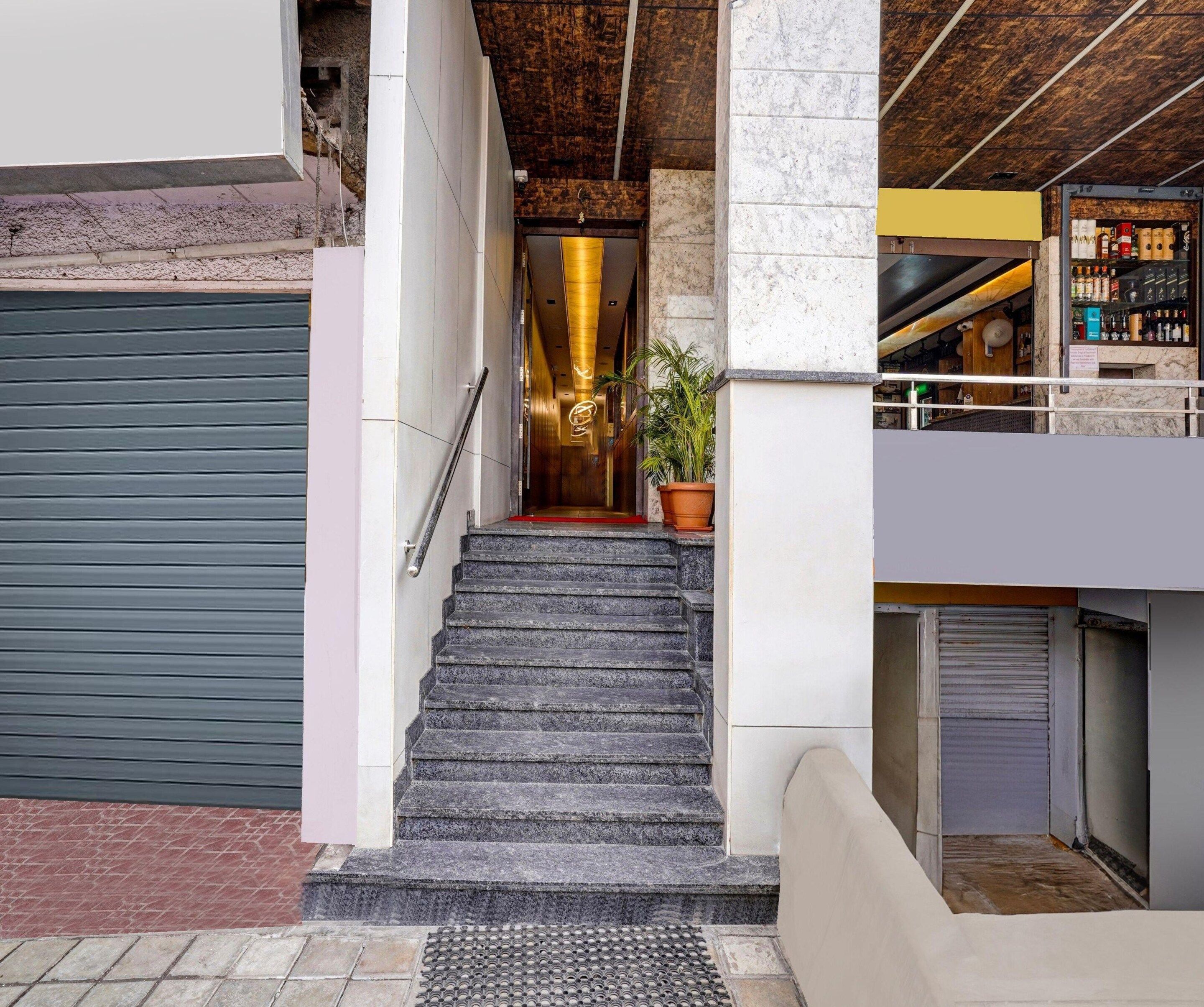 A staircase leading to a lobby with a potted plant, a closed shutter door, and a bar area with shelves.