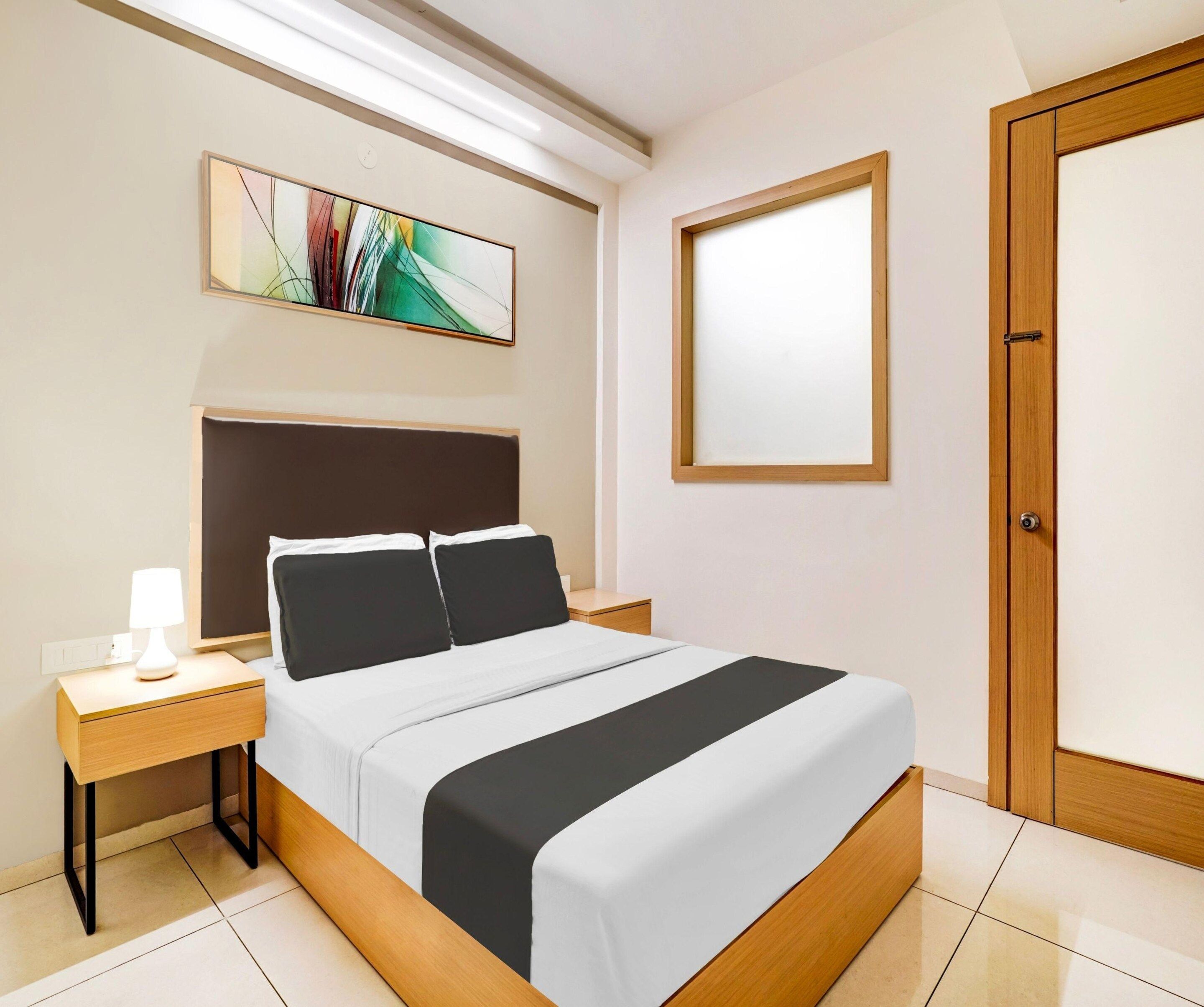 Een hotelkamer met een bed, nachtkastje, lamp, kunstwerk en een deur.