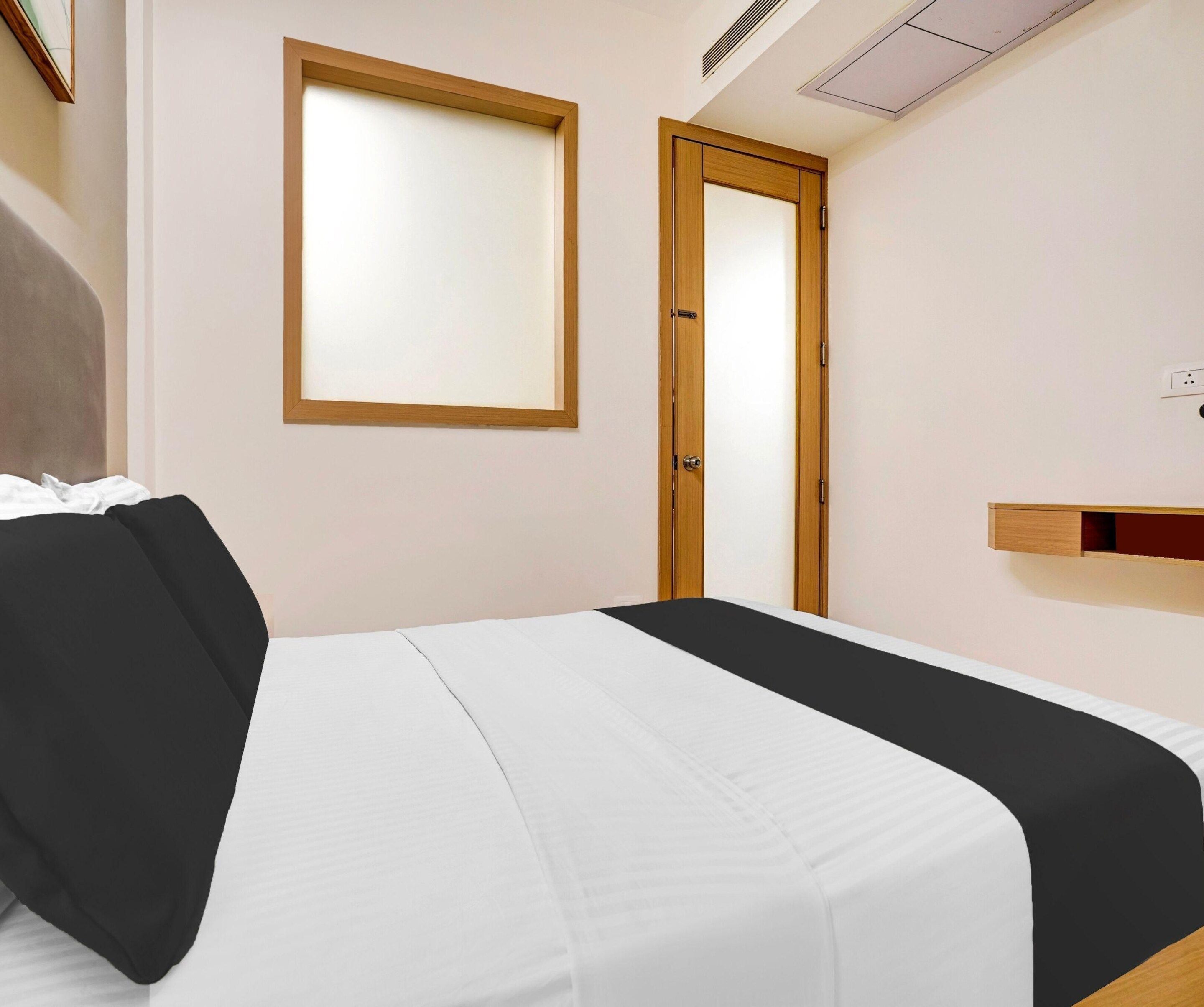A bedroom with a bed, a door, a window, and a wall-mounted shelf.