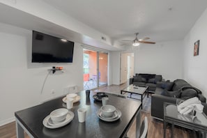 Ein modernes Wohnzimmer mit Flachbildfernseher, Deckenventilator und Essbereich mit Tisch für Zwei.