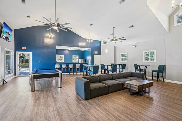 Una habitación amplia con mesa de billar, un sofá y varios ventiladores de techo.