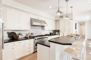 A modern kitchen with white cabinetry, a central island, stainless steel appliances, and pendant lighting. - Mins To Newport Beach, Pier, Water-Front Dining (Newport Beach)