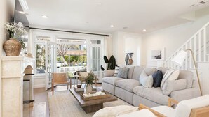 Ein modernes Wohnzimmer mit einer Couch, einem Couchtisch und Sesseln. Es gibt einen Kamin, ein Fenster mit Blick und eine Treppe.