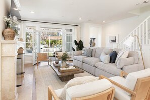 A modern living room with a sofa, coffee table, and chairs. There is a fireplace, a window with a view, and a staircase. - Mins To Newport Beach, Pier, Water-Front Dining (Newport Beach)