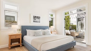 Ein Schlafzimmer mit einem großen Bett, Nachttischen, einem Fenster und Blick ins Freie.