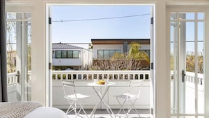 Ein Balkon mit weißer Reling, zwei weiße Stühle und ein runder Tisch mit einer Obstschale.