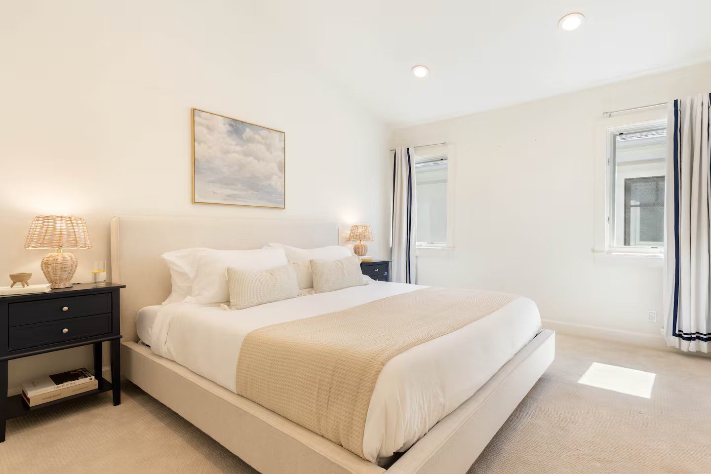 A bedroom with a bed, bedside tables, a nightstand, a wall-mounted lamp, a window with curtains, and a ceiling light.