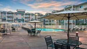 A poolside area with outdoor seating and umbrellas, surrounded by multi-story buildings.