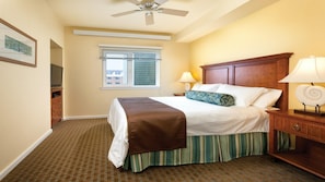 A hotel room with a bed, a nightstand, a lamp, a ceiling fan, a window, and a television.