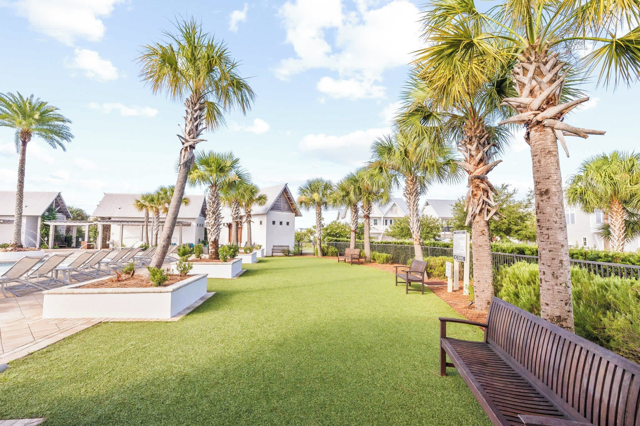 A well-maintained outdoor area with artificial grass, palm trees, and a wooden bench.