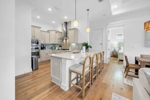 A modern kitchen with a central island, wooden chairs, and a dining area with a table and chairs. - Coastal Social by Stay on 30a (Watersound)