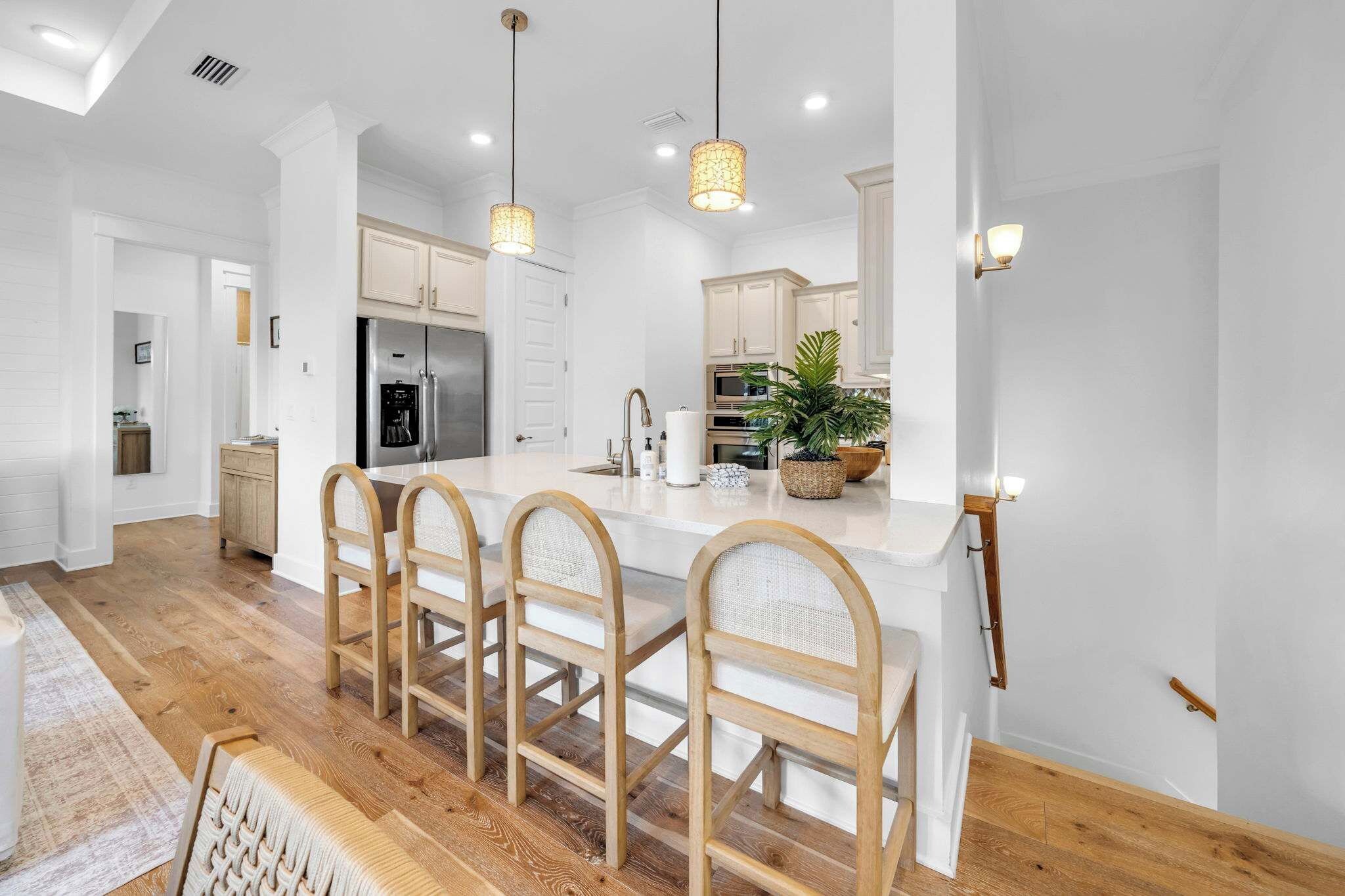 A modern kitchen with a central island, wooden chairs, and pendant lighting.