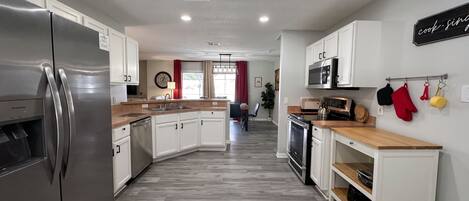 A modern kitchen with a stainless steel refrigerator, white cabinetry, a wooden countertop, and a microwave.