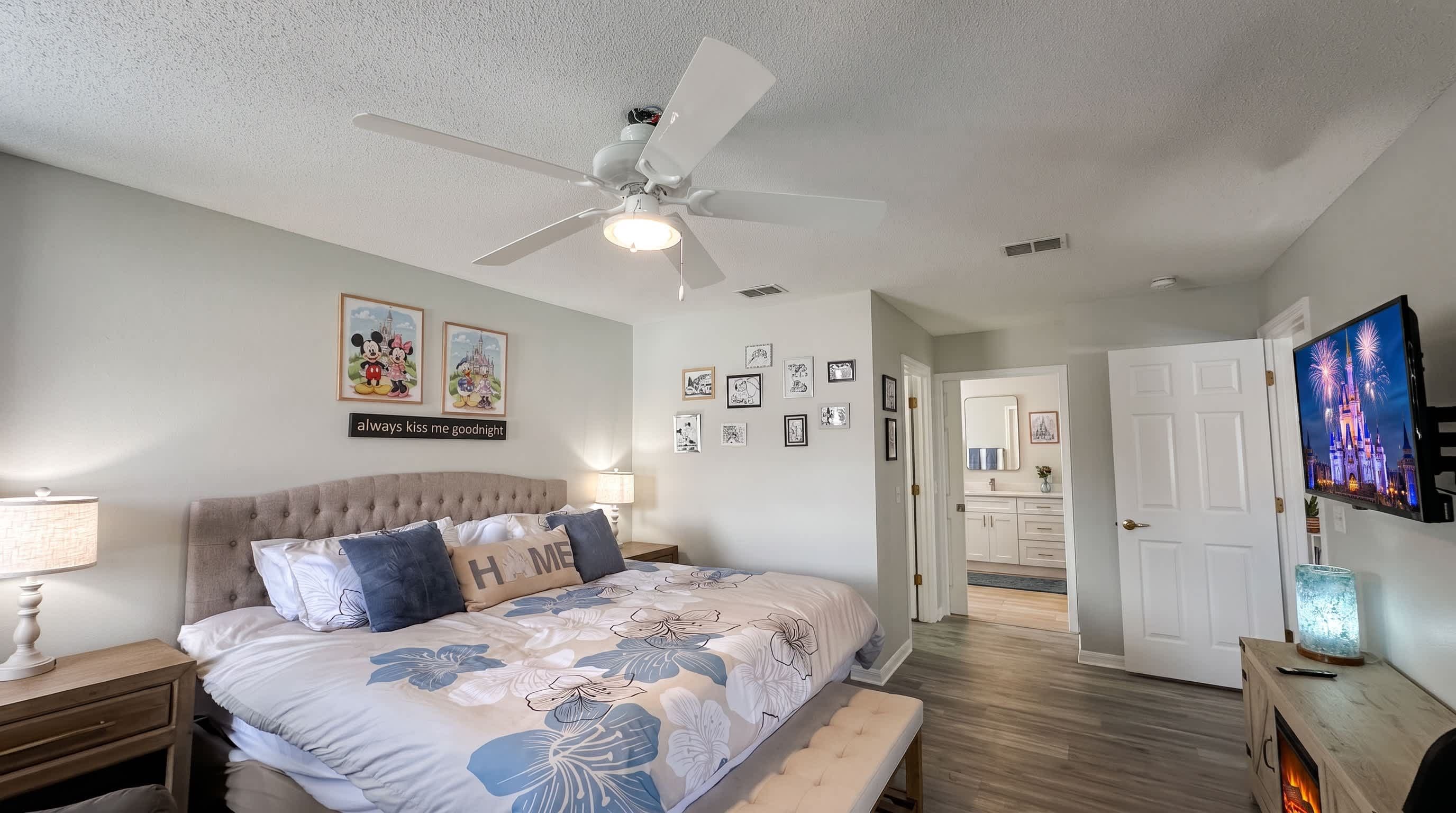 Un dormitorio con cama, ventilador de techo, decoración en la pared y televisor.