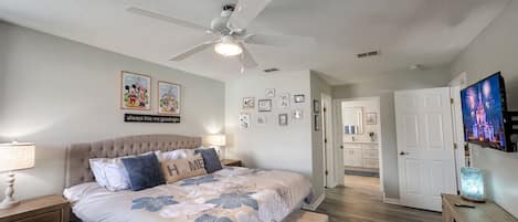 Un dormitorio con cama, ventilador de techo, decoración en la pared y televisor.