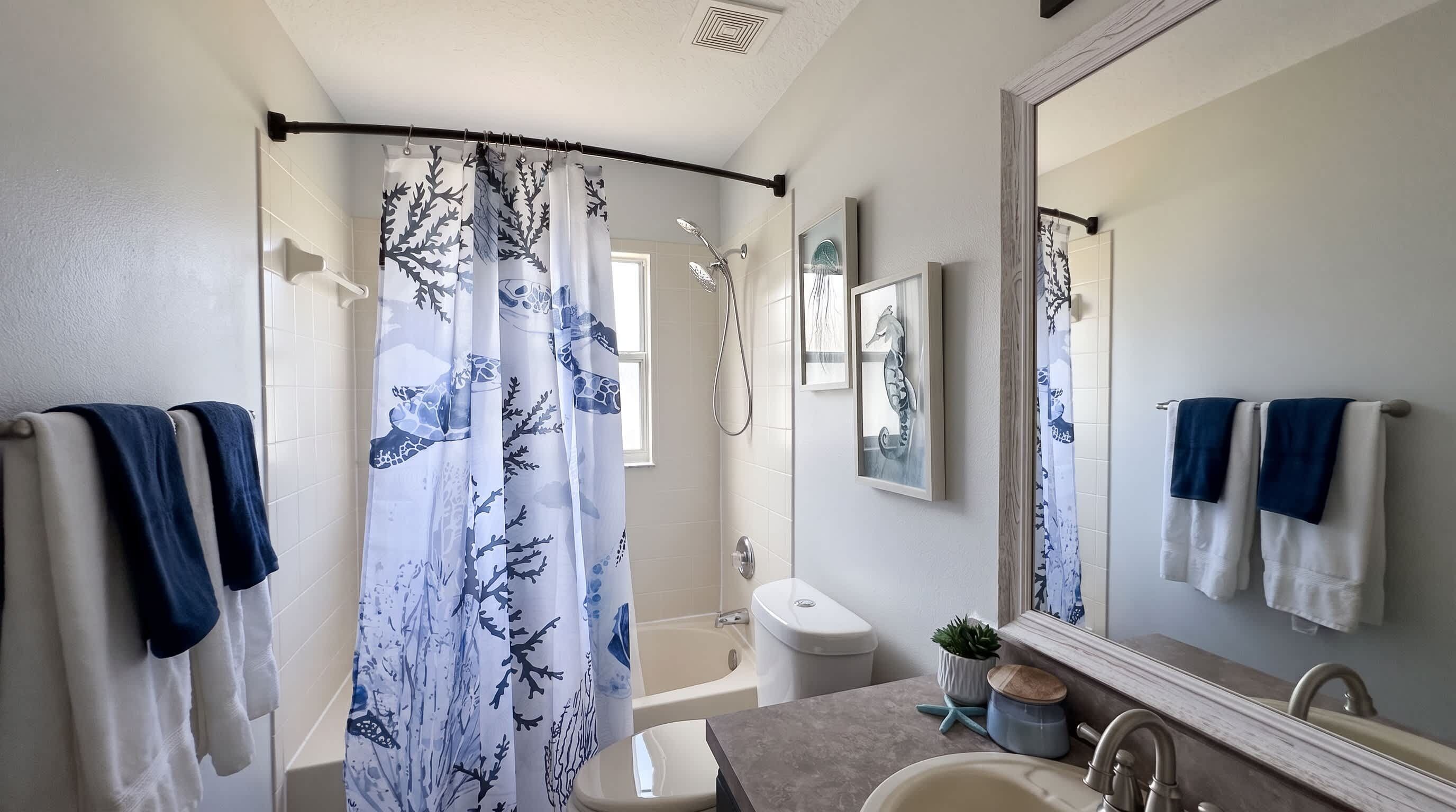 A bathroom with a shower curtain, a bathtub, a toilet, a sink, and a mirror.