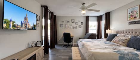 Een hotelkamer met een grote flatscreen-tv, een bed met een gestoffeerd hoofdeinde, een bureau met stoel, een open haard en een plafondventilator.