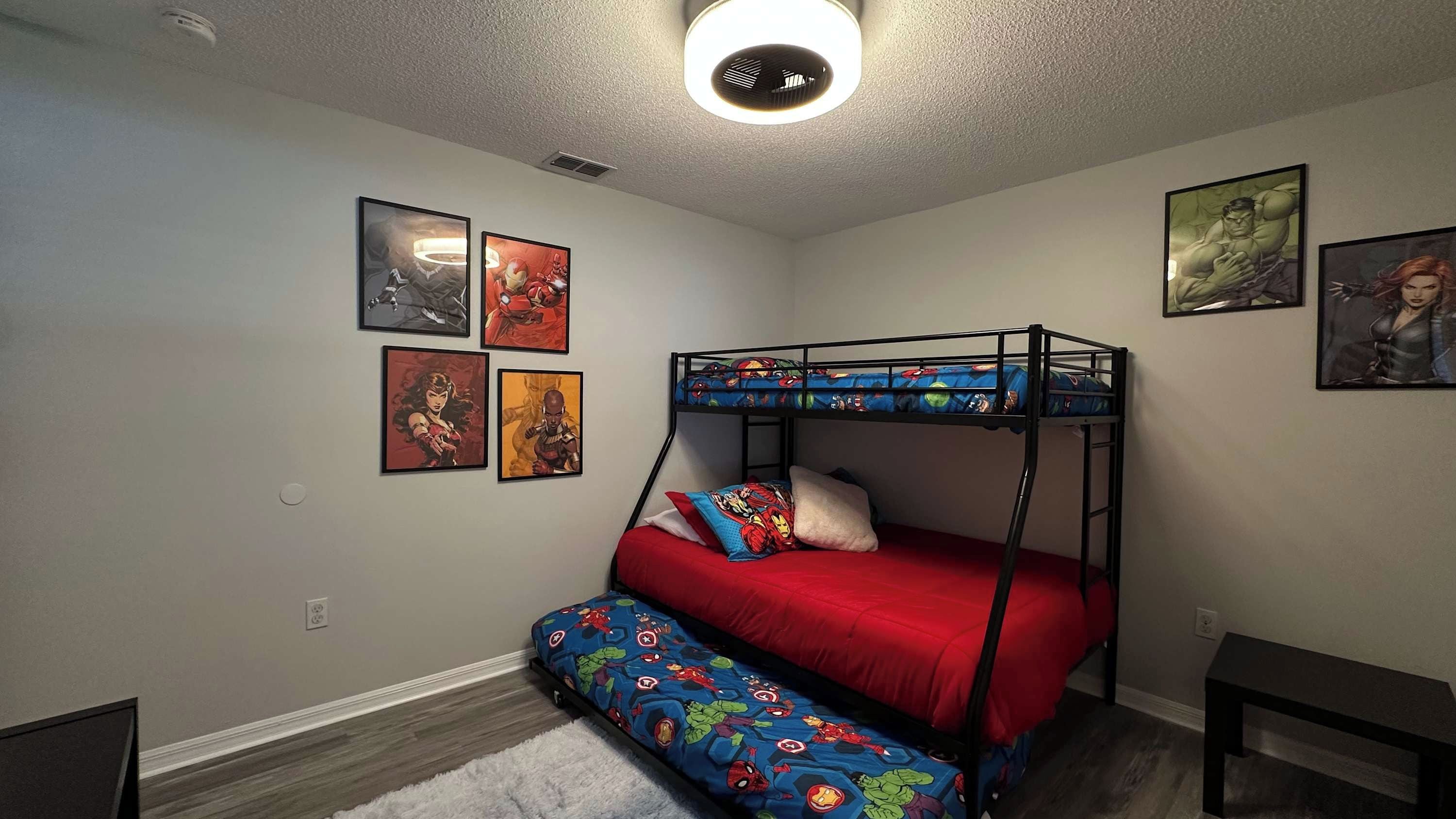 A bunk bed with a red mattress and patterned bedding, a ceiling light, and four framed comic book covers on the wall.