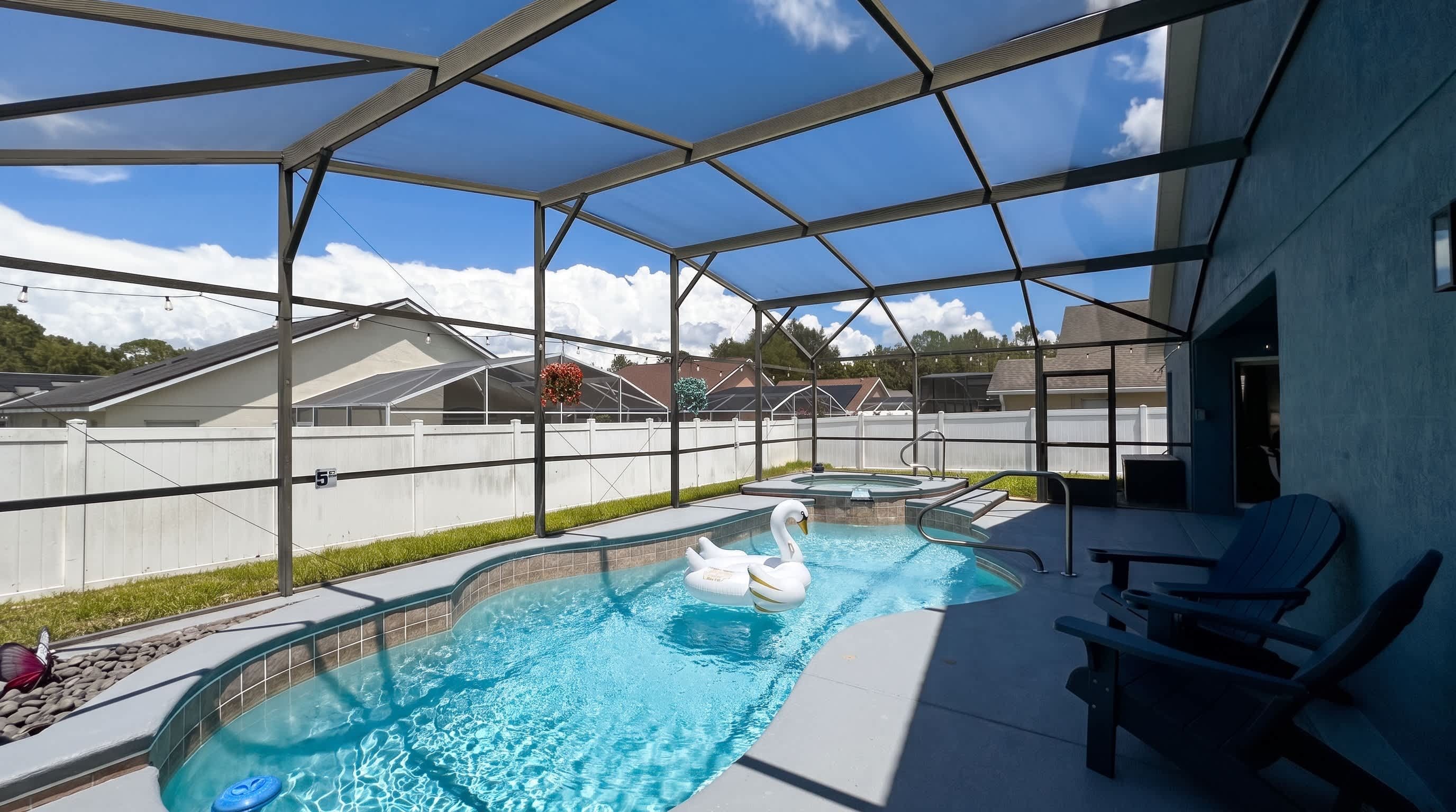 An outdoor swimming pool with a white swan float, surrounded by a covered patio area with chairs.