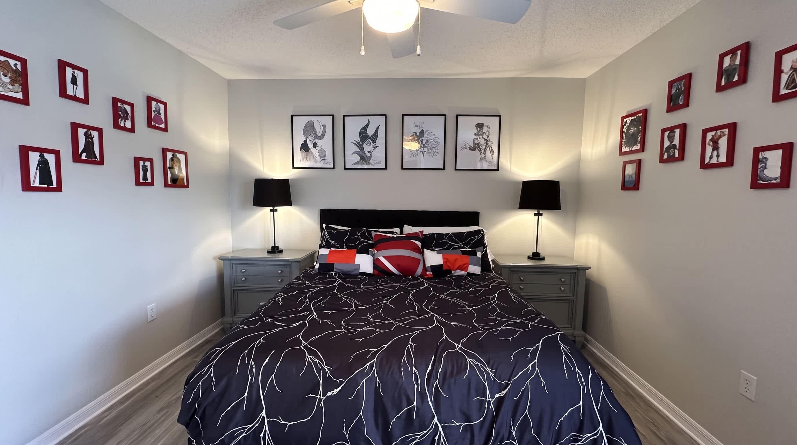 Een slaapkamer met een bed, twee nachtkastjes met lampen, een plafondventilator en ingelijste foto's aan de muur.