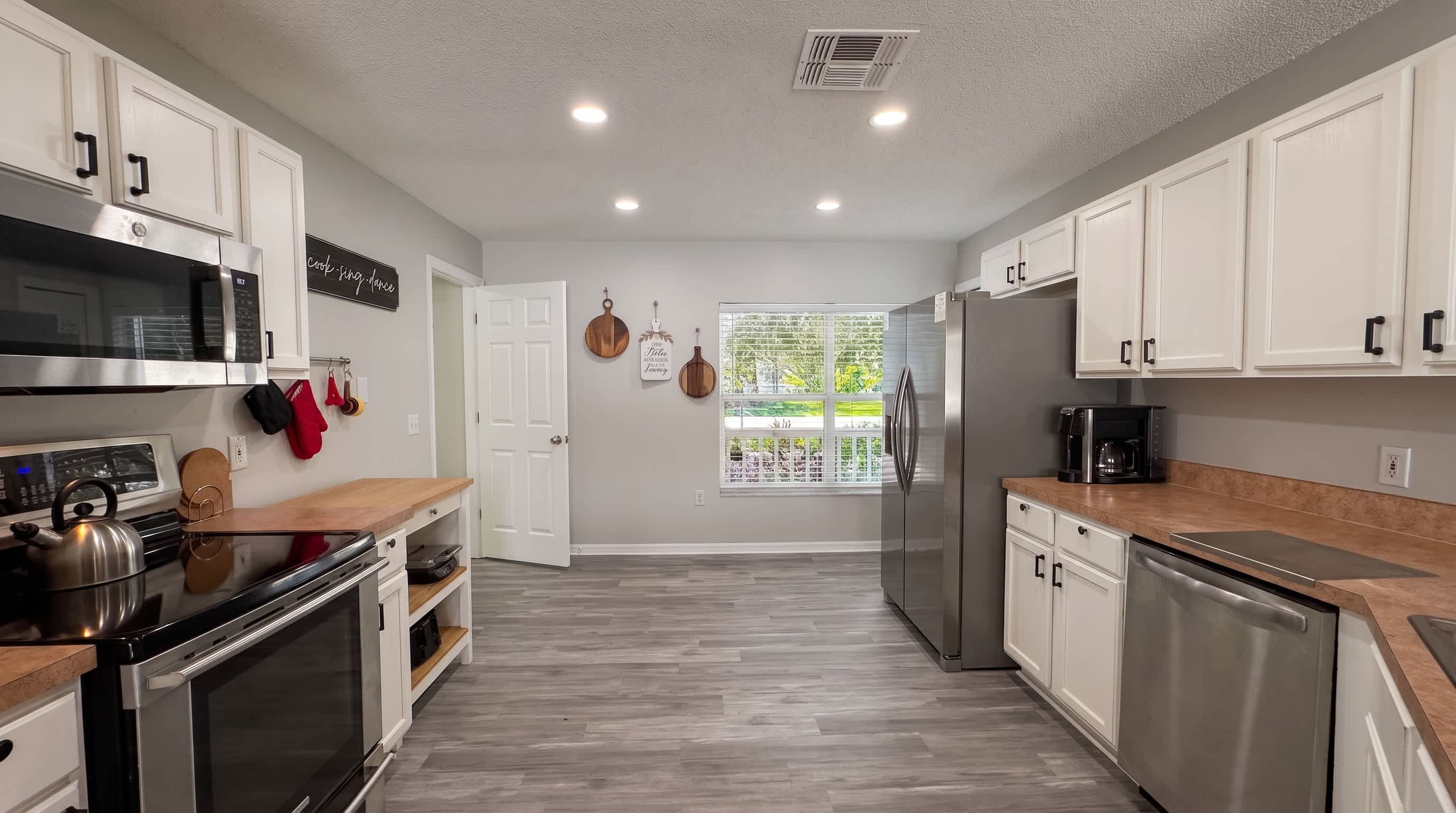 A modern kitchen with stainless steel appliances, white cabinetry, and a window with a view of greenery.