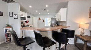 A modern kitchen with a central island, bar stools, and a dining table with a lamp. - Starlight and Shells - Pool (Davenport)