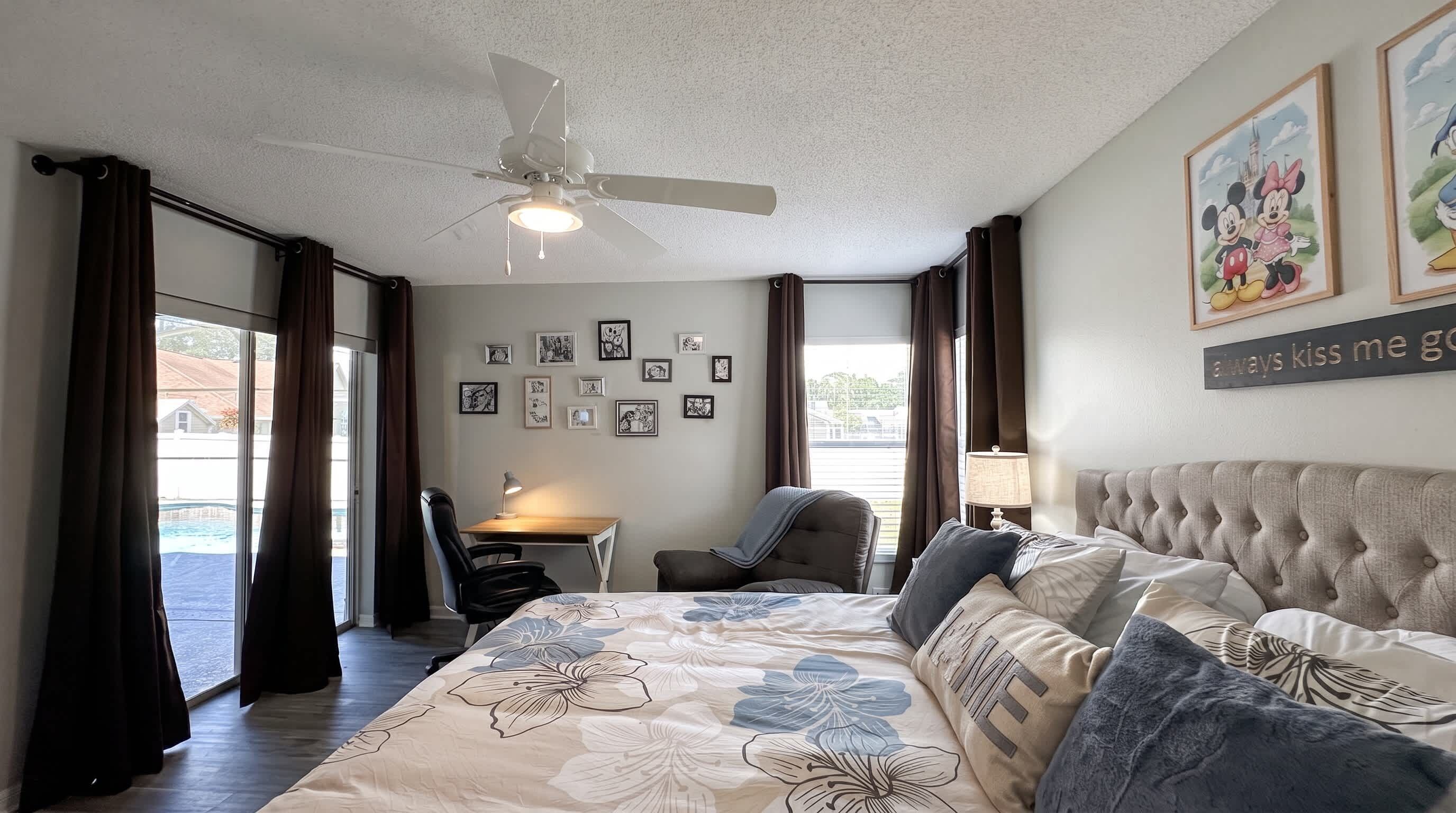 A hotel room with a bed, a desk, a chair, and a ceiling fan.