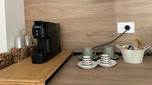 A coffee machine on a wooden counter with cups and a basket of items.
