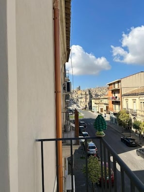 Un balcón con vista a una calle de la ciudad, edificios y un cielo despejado.