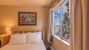 Un dormitorio con cama, mesita de noche, lámpara, un cuadro y una ventana con cortinas.